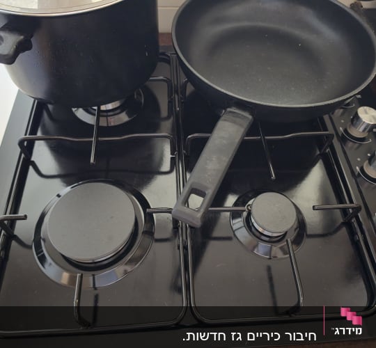 כיריים גז שחורות מותקנות במטבח עם סיר ומחבת עליהן